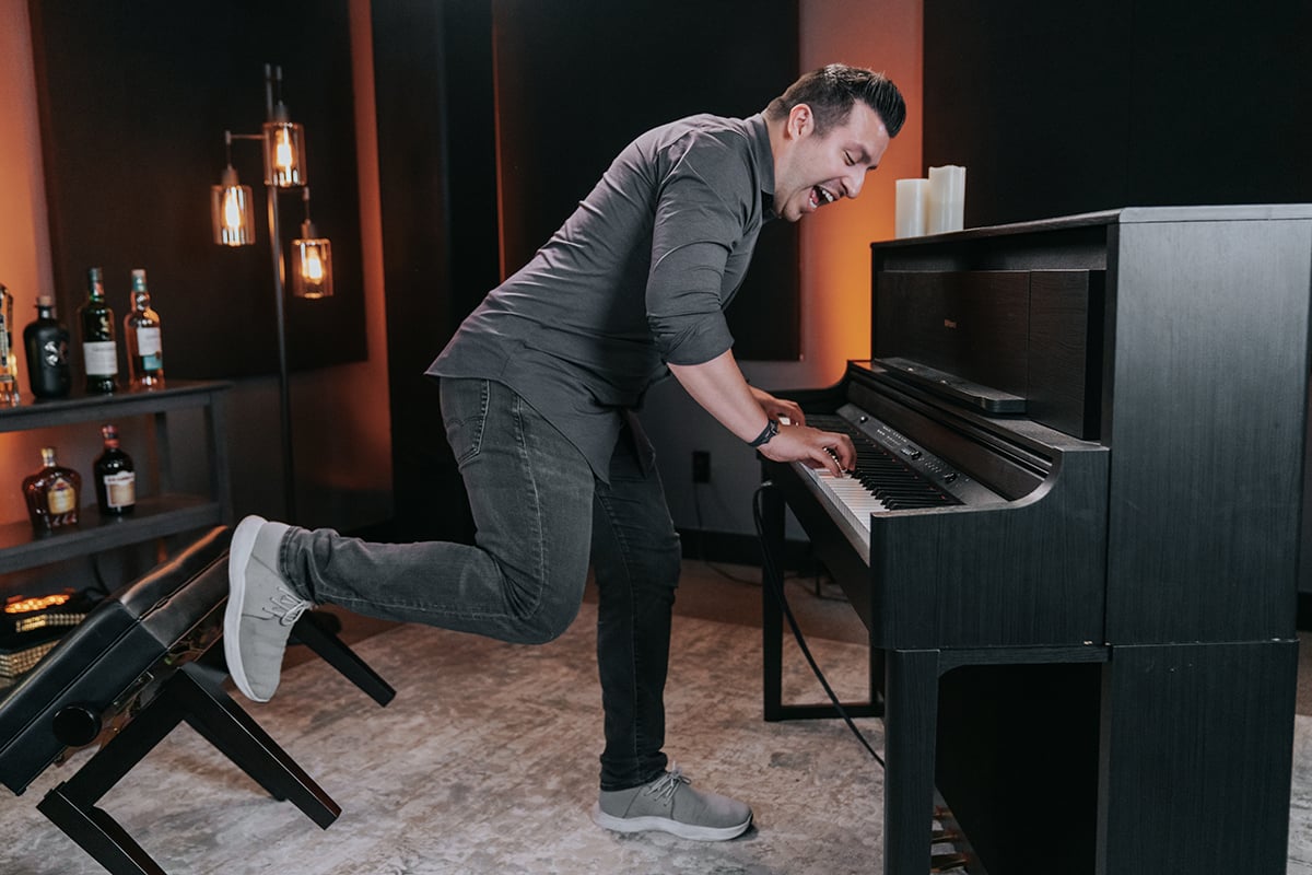 Man playing upright piano standing up kicking back chair.