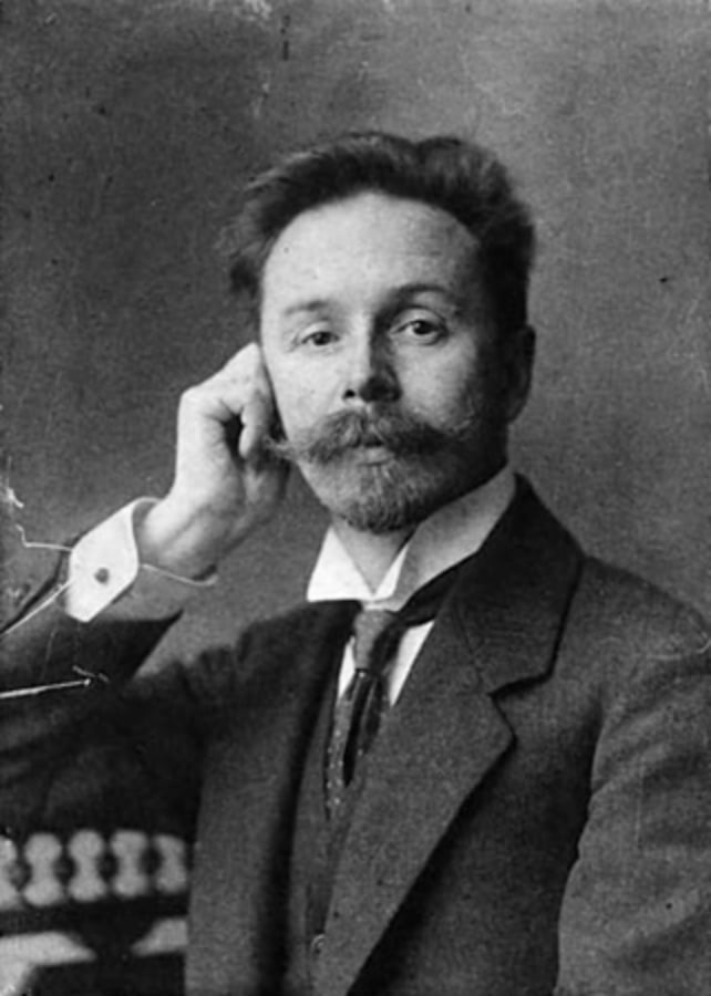 Monotone photo of man with handlebar mustache looking thoughtful with head resting on hand.